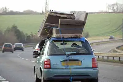 a photo of a small hatchback car with a sofa on the luggage rack