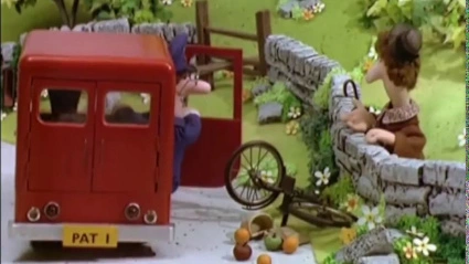 A bicycle in the road with fruit scattered, with postman pat's van door open, as he exchanges words with a woman over the wall