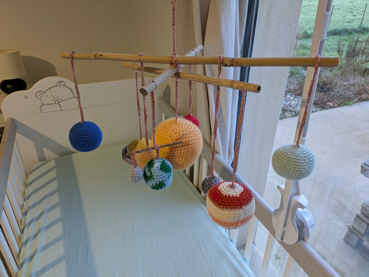 Un mobile pour enfant réalisé en crochet, représentant le système solaire. Il est accroché au dessus d'un lit à barreaux.