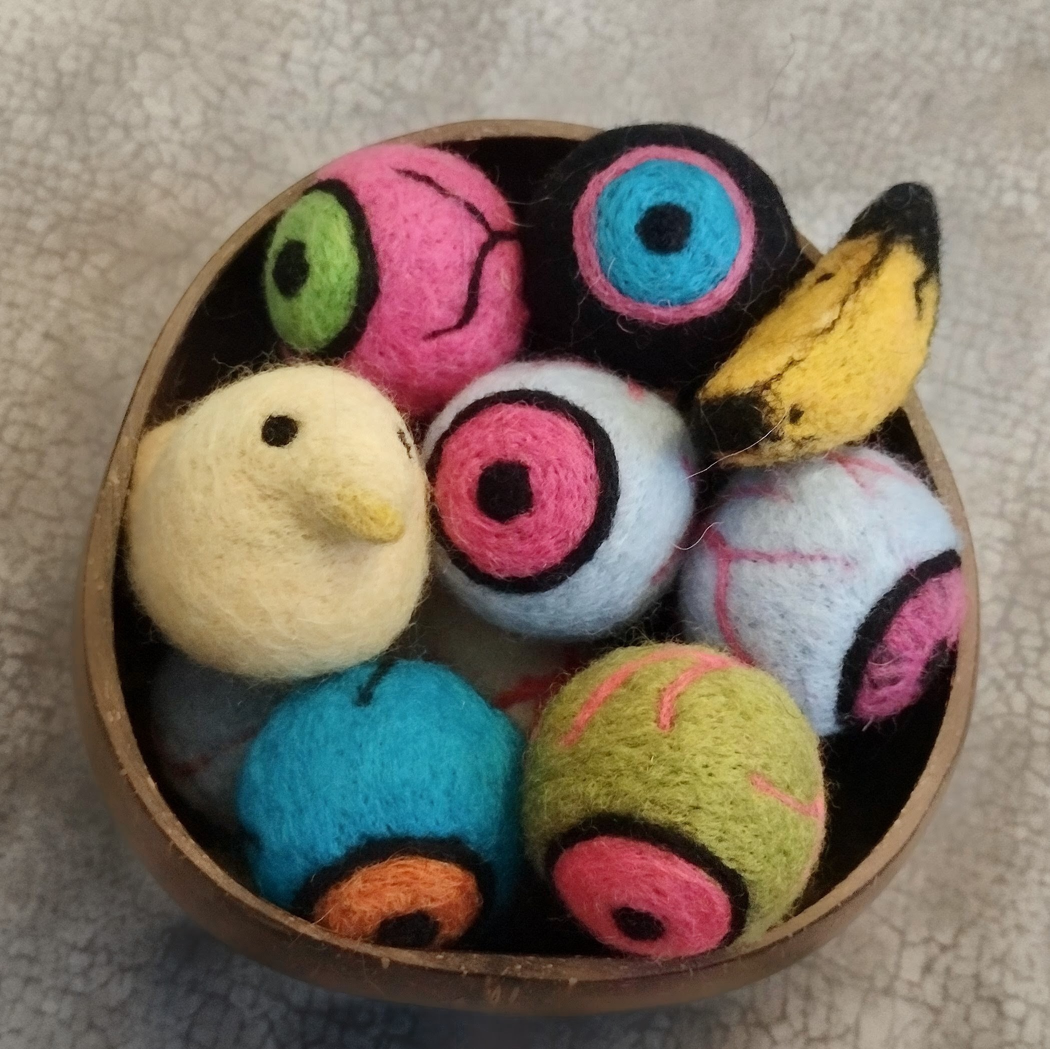 A bowl of colourful felted objects, mostly eyeballs, with a banana and a peep.