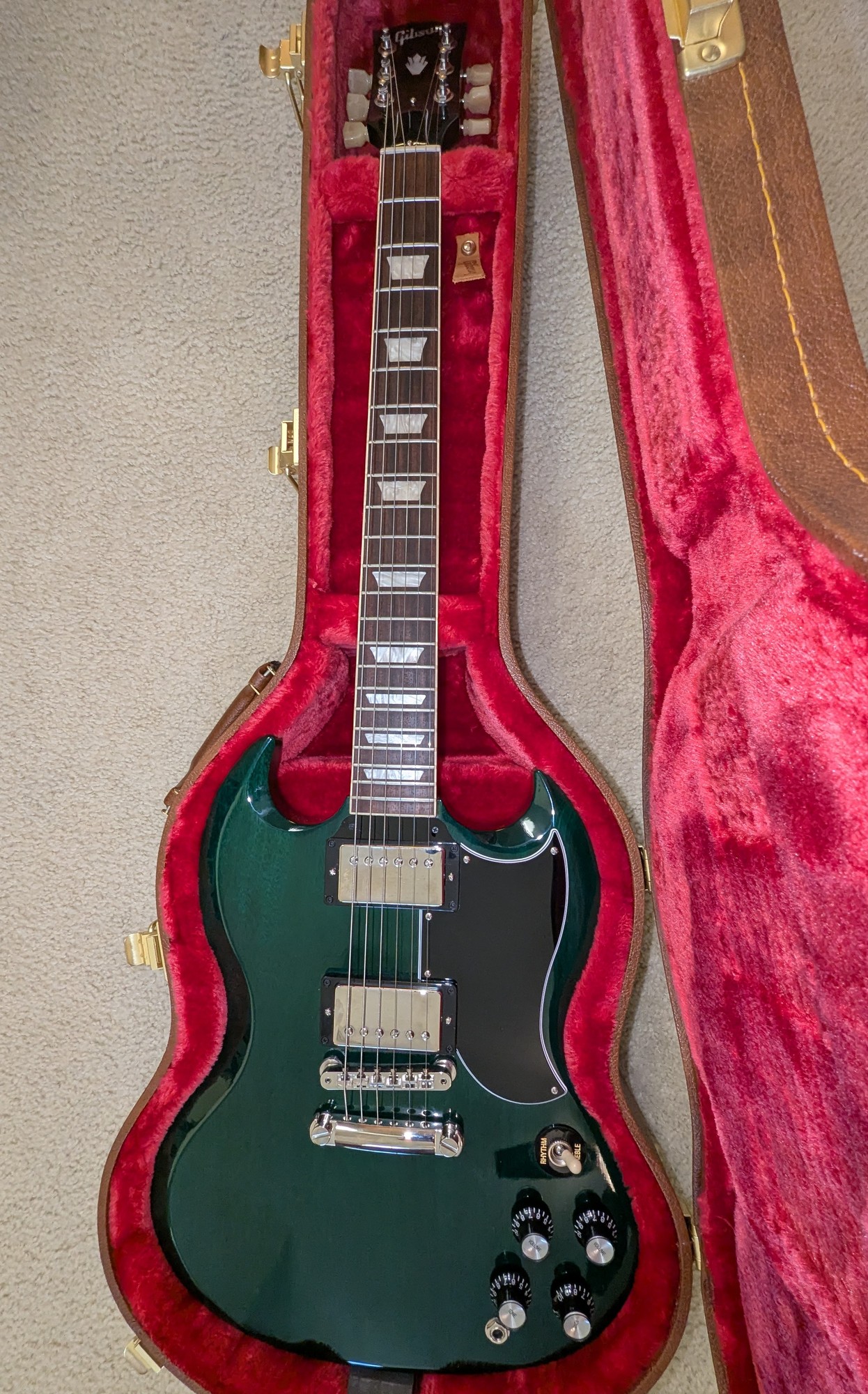 A Gibson SG guitar with green body in a brown hard shell case with a plush red interior.