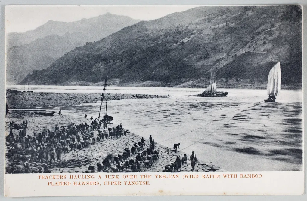 River scene, several teams of people pulling ropes attached to boats in the river