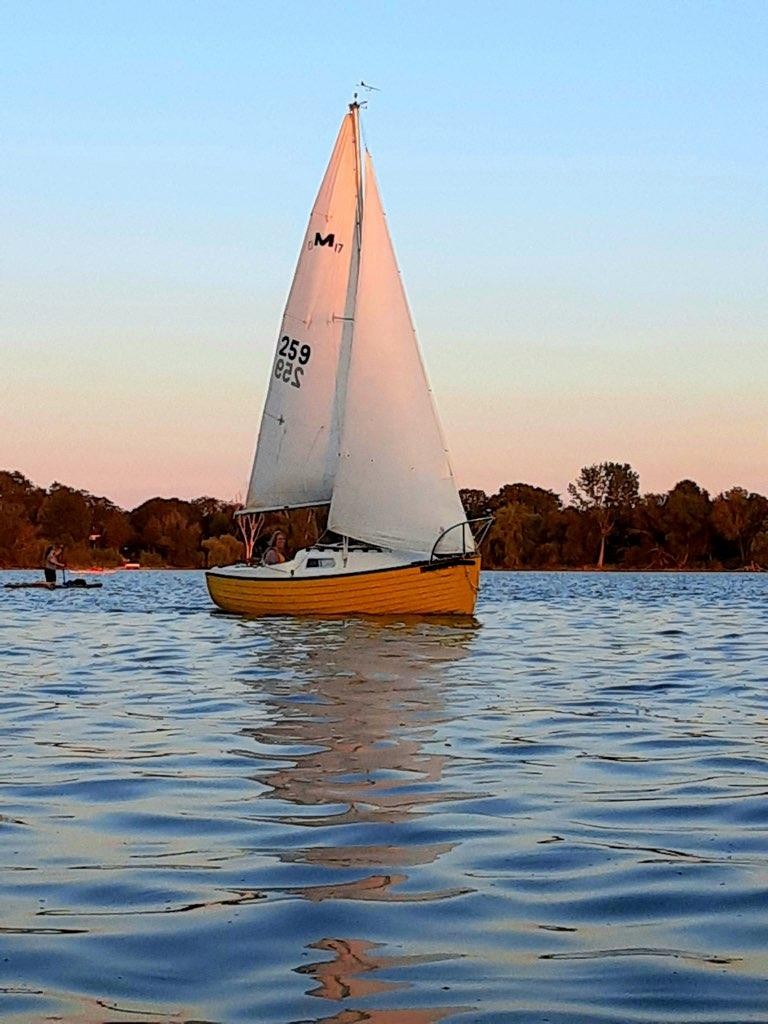 Cute yellow sailboat at sunset, sailing diagonally towards viewer under full main and working jib.