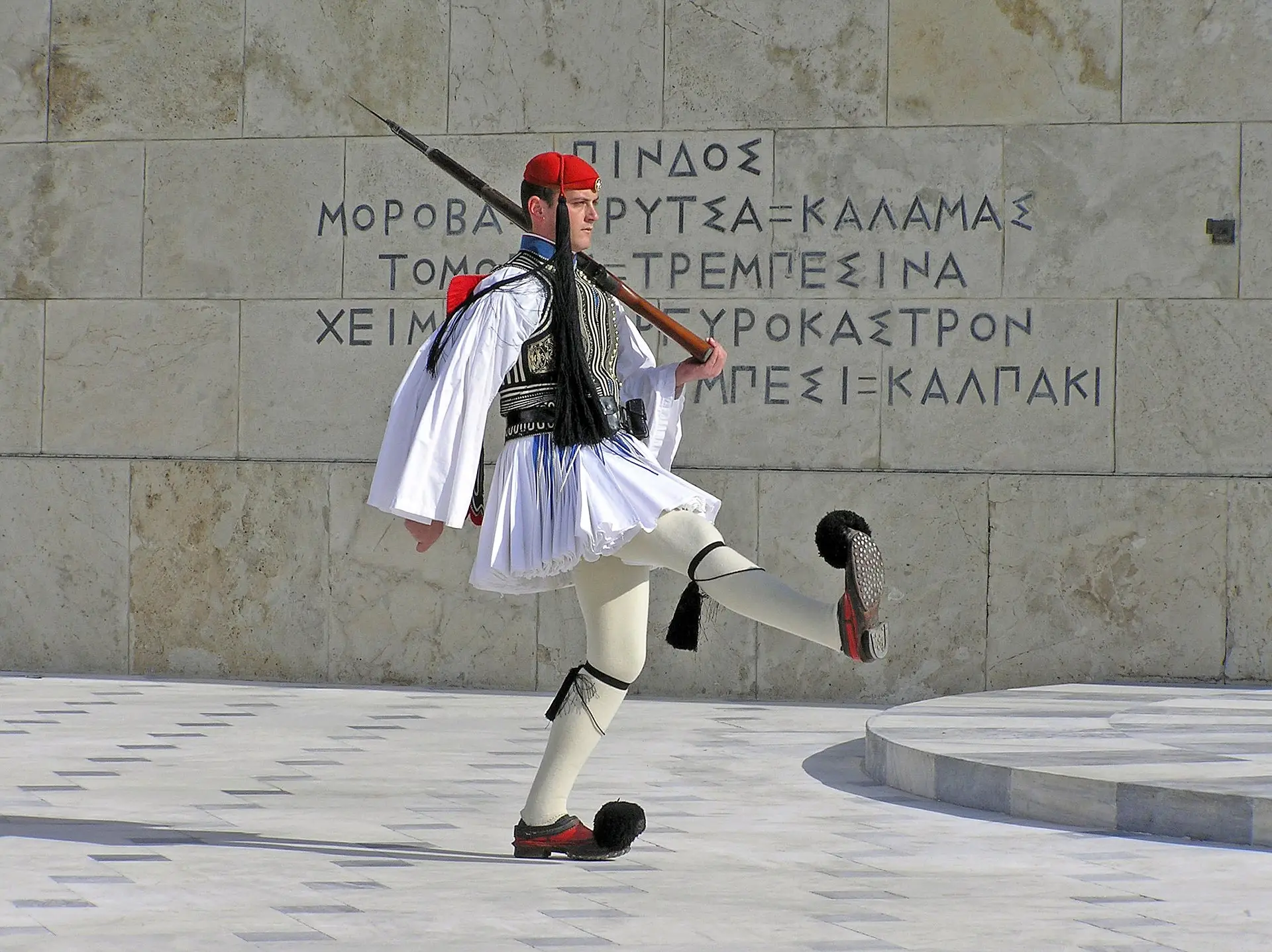 Greek Presidential Guard, wearing a pretty white skirt, white leggings, and shoes with black pom-poms on the toes.