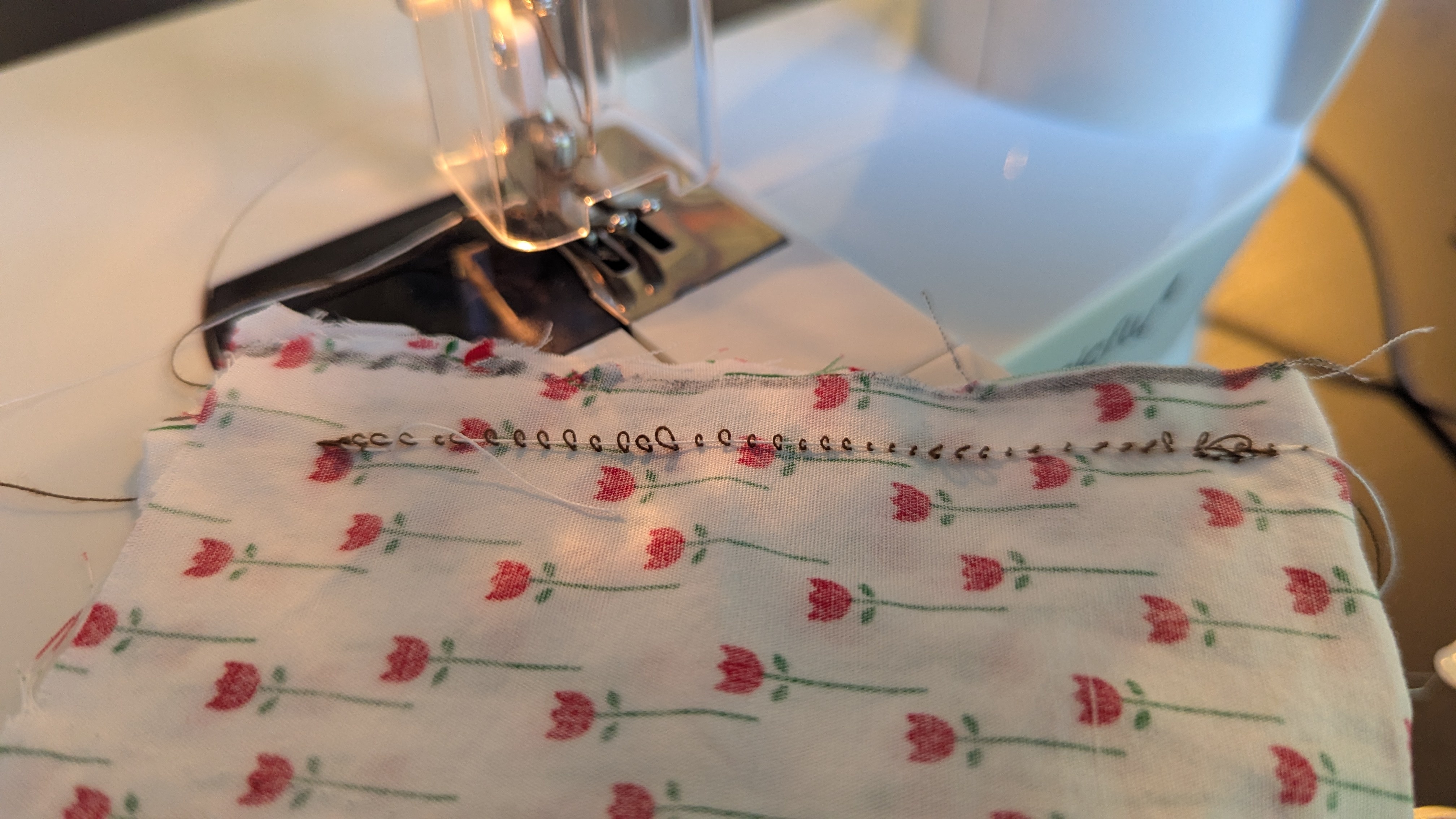 a piece of test fabric on a small sewing machine with a straight line of stitches. the loops are loose. 