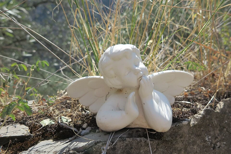 Plaster statue of a cherub, located within a garden.