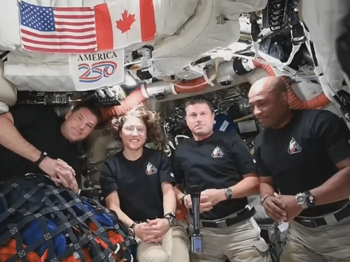 The Artemis II crew smile and look ahead while the microphone floats in the middle between the four of them